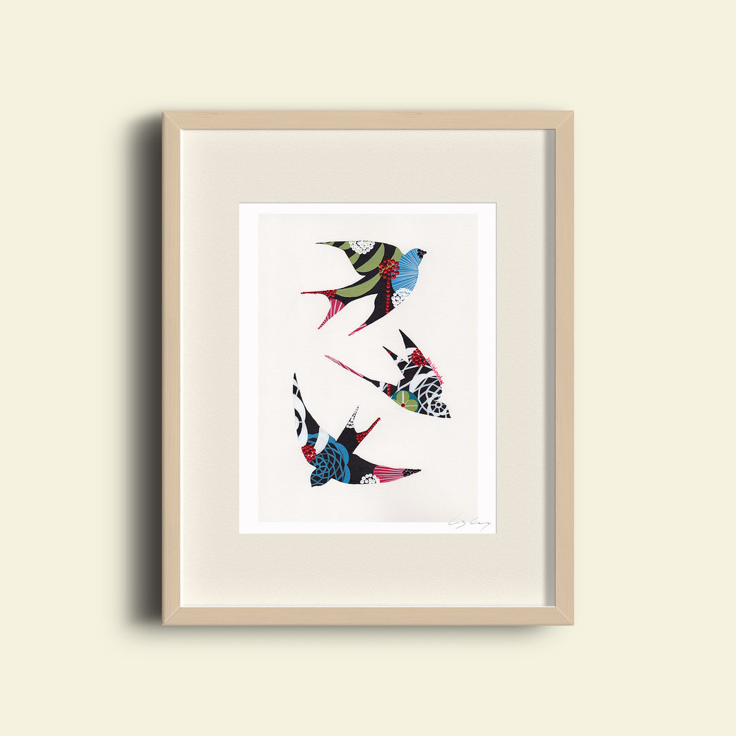 A framed fine art print, by Lis Gonçalves. Open edition, signed by the artist (printed in Hahnemühle matt fibre paper) featuring a colorful swallows illustration on a beige wall