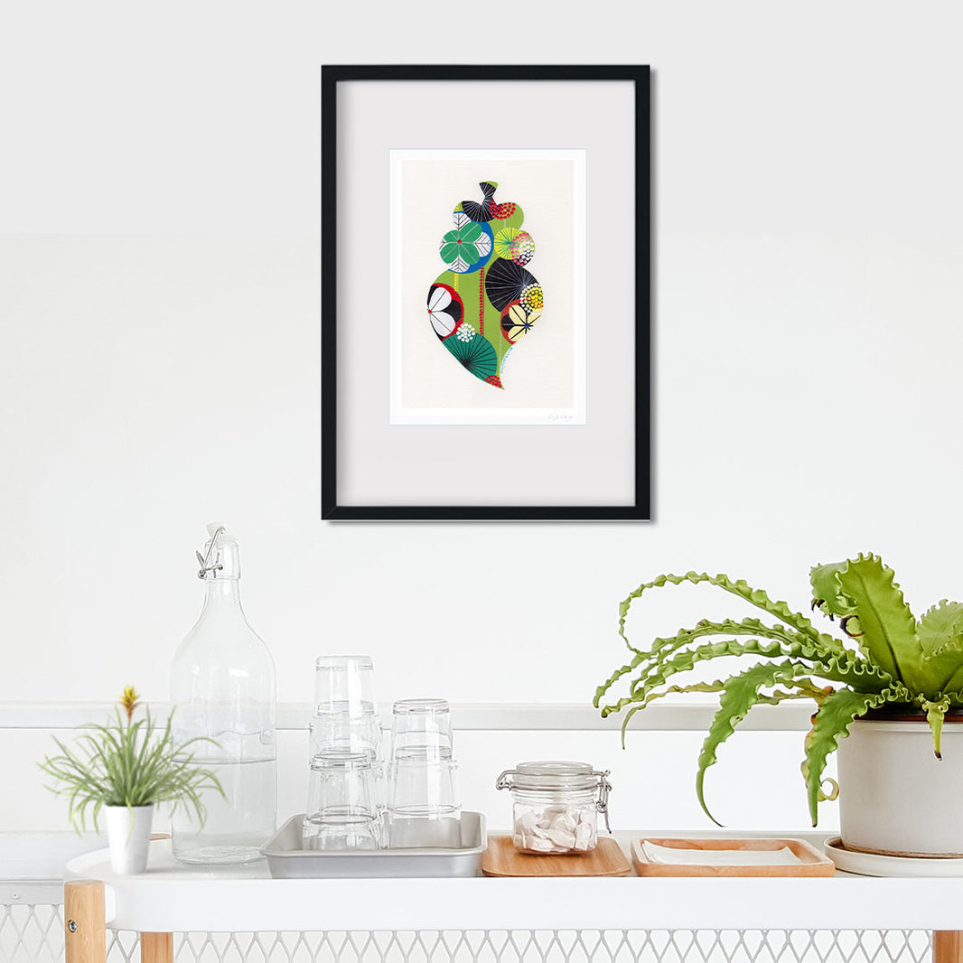 A framed fine art print, by Lis Gonçalves. Open edition, signed by the artist (printed in Hahnemühle matt fibre paper) featuring a colorful Portuguese Viana heart on a wall above a kitchen counter with plants.