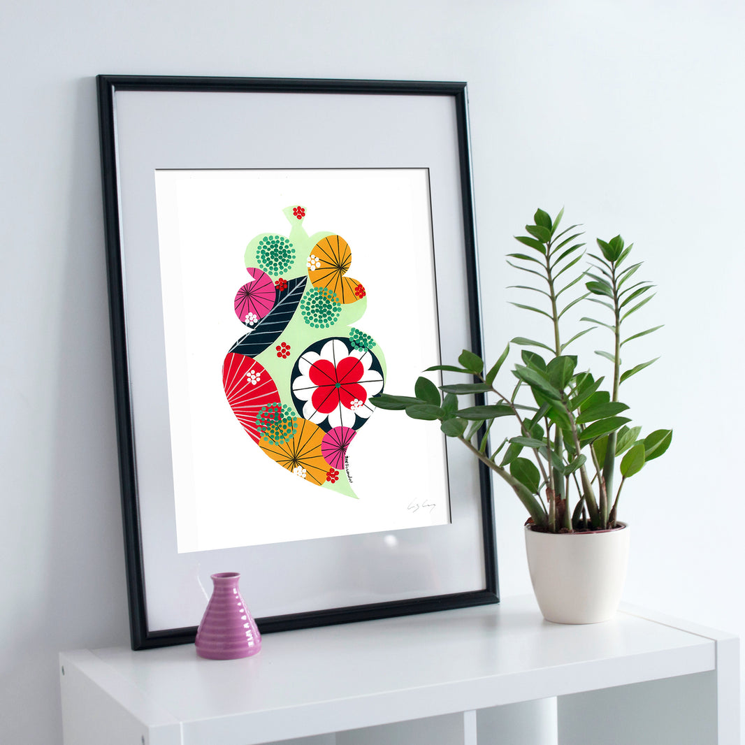 A framed fine art print, by Lis Gonçalves. Open edition, signed by the artist (printed in Hahnemühle matt fibre paper) featuring a colorful Portuguese Viana heart on a white surface with a plant and small vase.