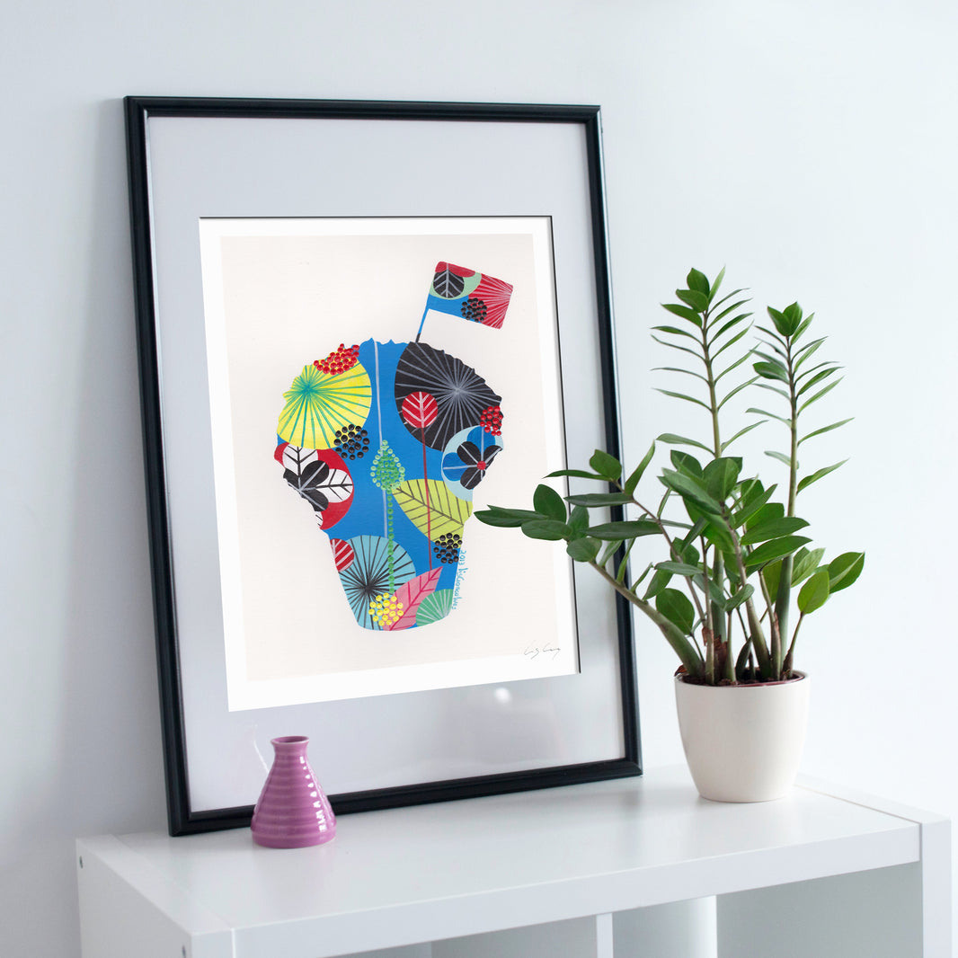A framed fine art print, by Lis Gonçalves. Open edition, signed by the artist (printed in Hahnemühle matt fibre paper) featuring a colorful, patterned manjerico basil plant illustration leaning on a white table next to a potted green plant and a small pink vase against a white wall.