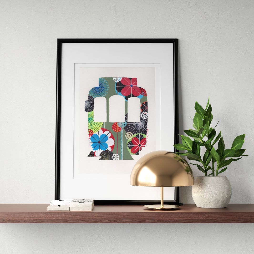 A framed fine art print, by Lis Gonçalves. Open edition, signed by the artist (printed in Hahnemühle matt fibre paper) featuring a colorful Lisbon tram on a wooden shelf with a gold lamp and plant.