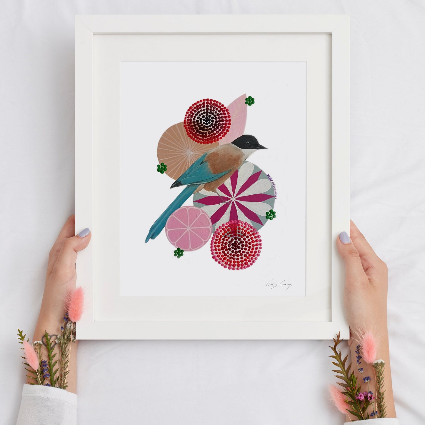 A framed fine art print, by Lis Gonçalves. Open edition, signed by the artist. Printed in Hahnemühle matt fibre paper;  featuring a stylized magpie and geometric floral motifs in pink, red, blue, beige, and green, held by two hands against a white fabric background.