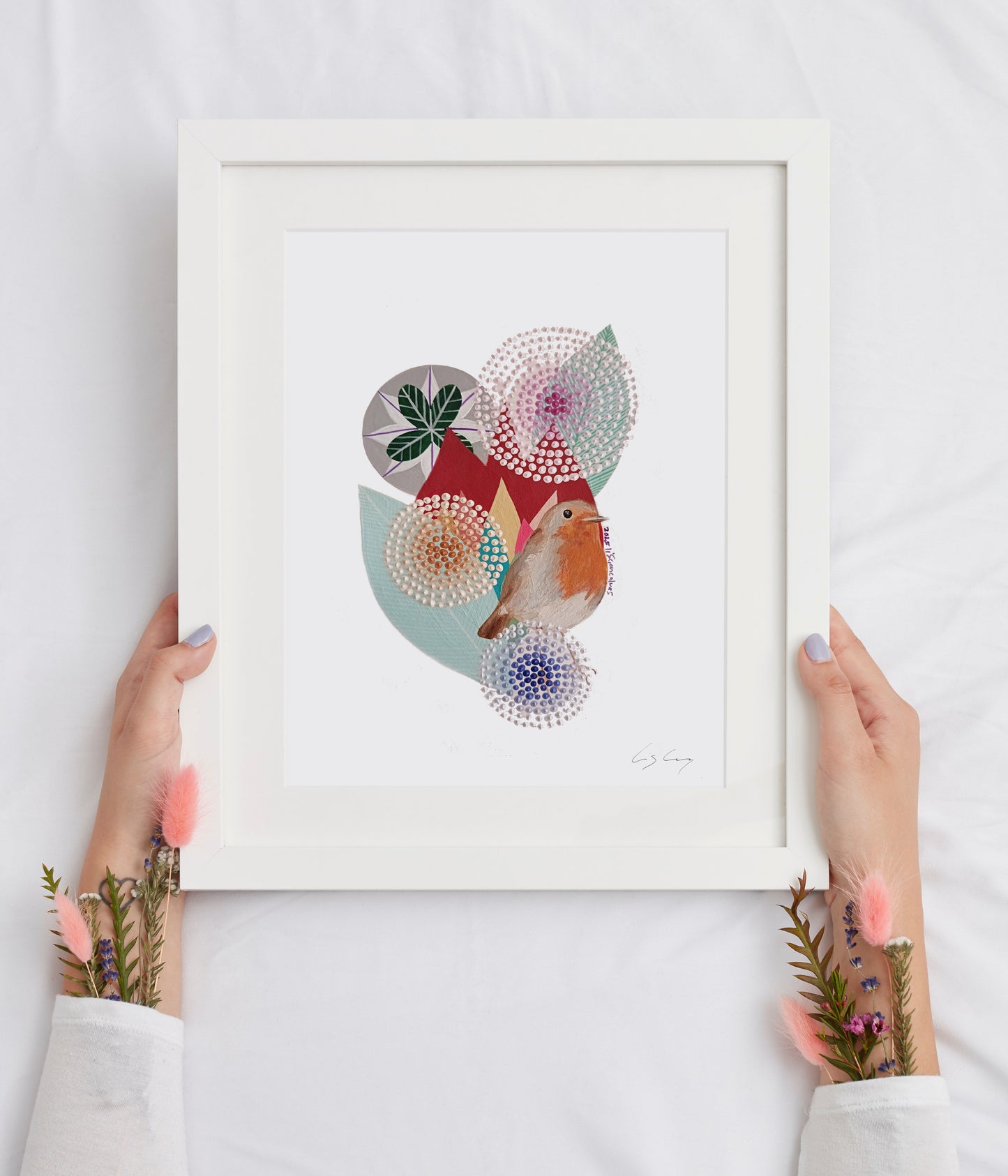 A framed fine art print, by Lis Gonçalves. Open edition, signed by the artist. Printed in Hahnemühle matt fibre paper; featuring a robin bird and abstract geometric shapes in pastel colors, held by two hands against a white fabric background.