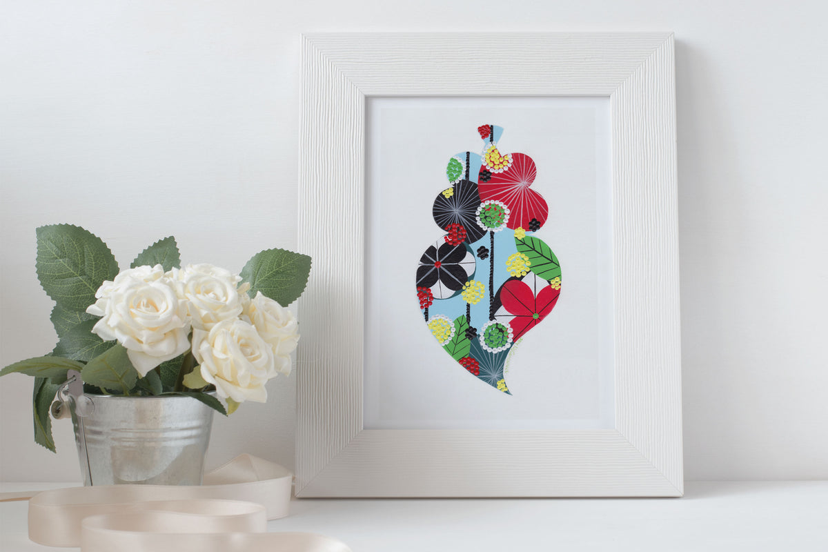 A framed fine art print, by Lis Gonçalves. Open edition, signed by the artist (printed in Hahnemühle matt fibre paper) featuring a colorful Portuguese Viana heart on a white surface with a potted plant.