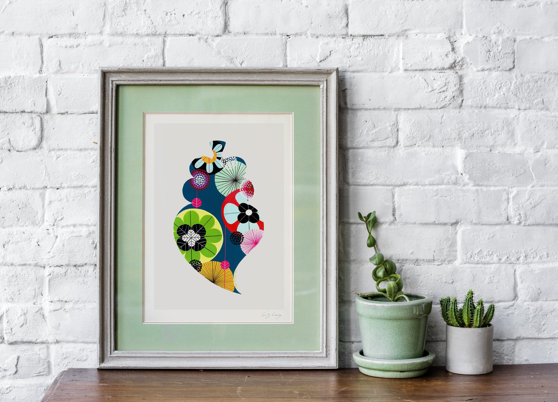 A framed fine art print, by Lis Gonçalves. Open edition, signed by the artist (printed in Hahnemühle matt fibre paper) featuring a colorful Portuguese Viana heart on a white brick wall with potted plants.