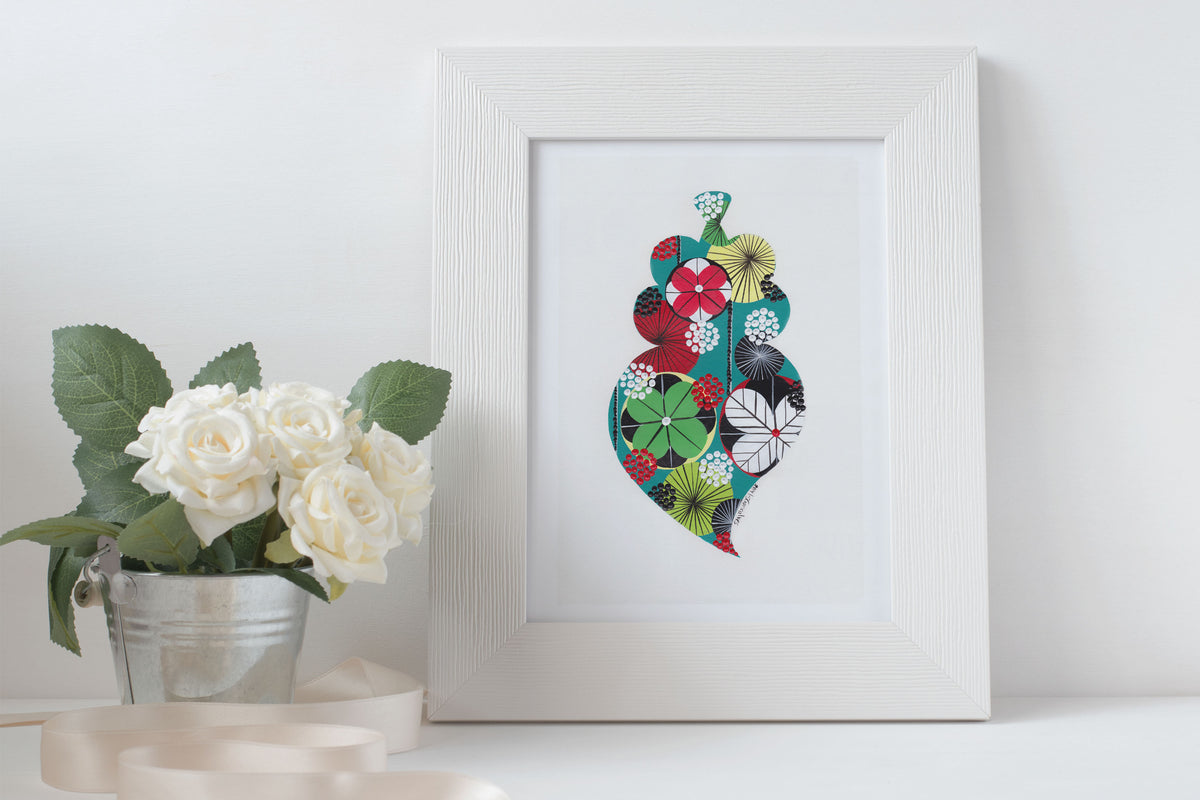 A framed fine art print, by Lis Gonçalves. Open edition, signed by the artist (printed in Hahnemühle matt fibre paper) featuring a colorful Portuguese Viana heart with a potted plant on a white surface