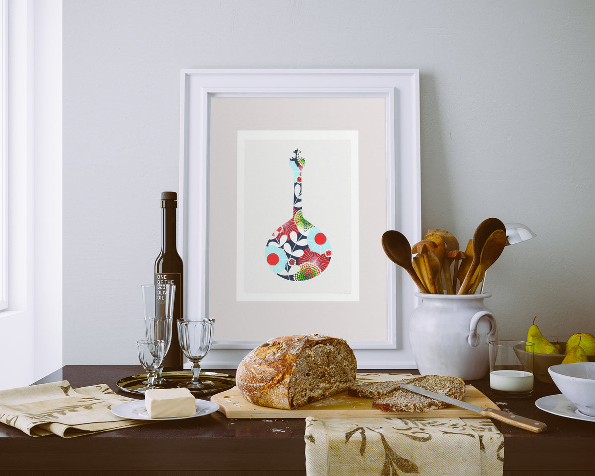 A framed fine art print, by Lis Gonçalves. Open edition, signed by the artist (printed in Hahnemühle matt fibre paper) featuring a colorful Portuguese guitar, in a dining table setup with bread, wine, and a colorful guitar painting on the wall.