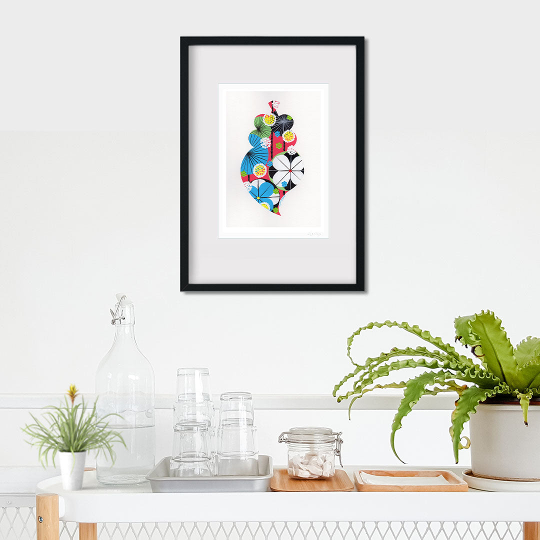 A framed fine art print, by Lis Gonçalves. Open edition, signed by the artist (printed in Hahnemühle matt fibre paper) featuring a colorful Portuguese Viana heart on a white wall with plants and decor below.