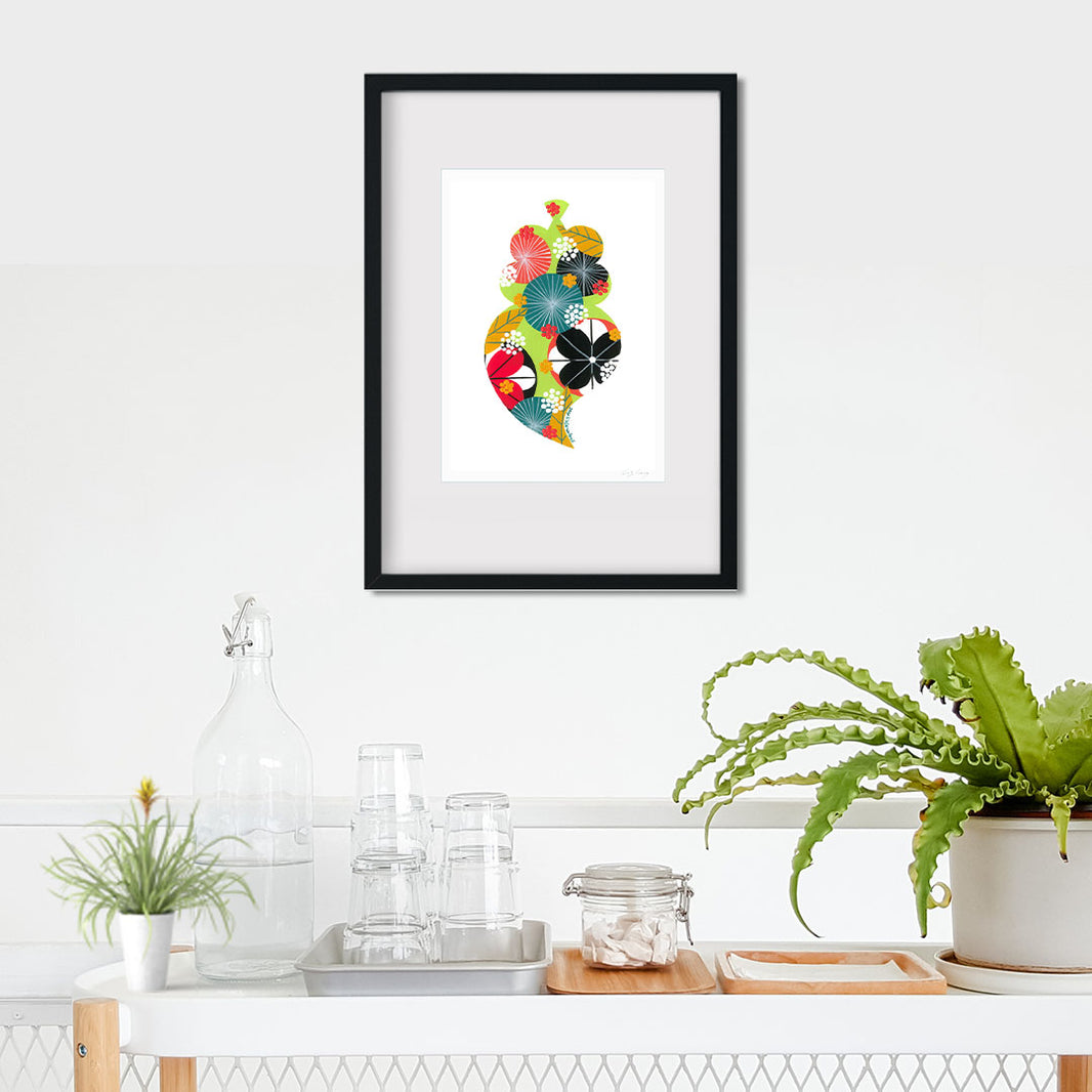 A framed fine art print, by Lis Gonçalves. Open edition, signed by the artist (printed in Hahnemühle matt fibre paper) featuring a colorful Portuguese Viana heart on a white wall with plants and decor below.