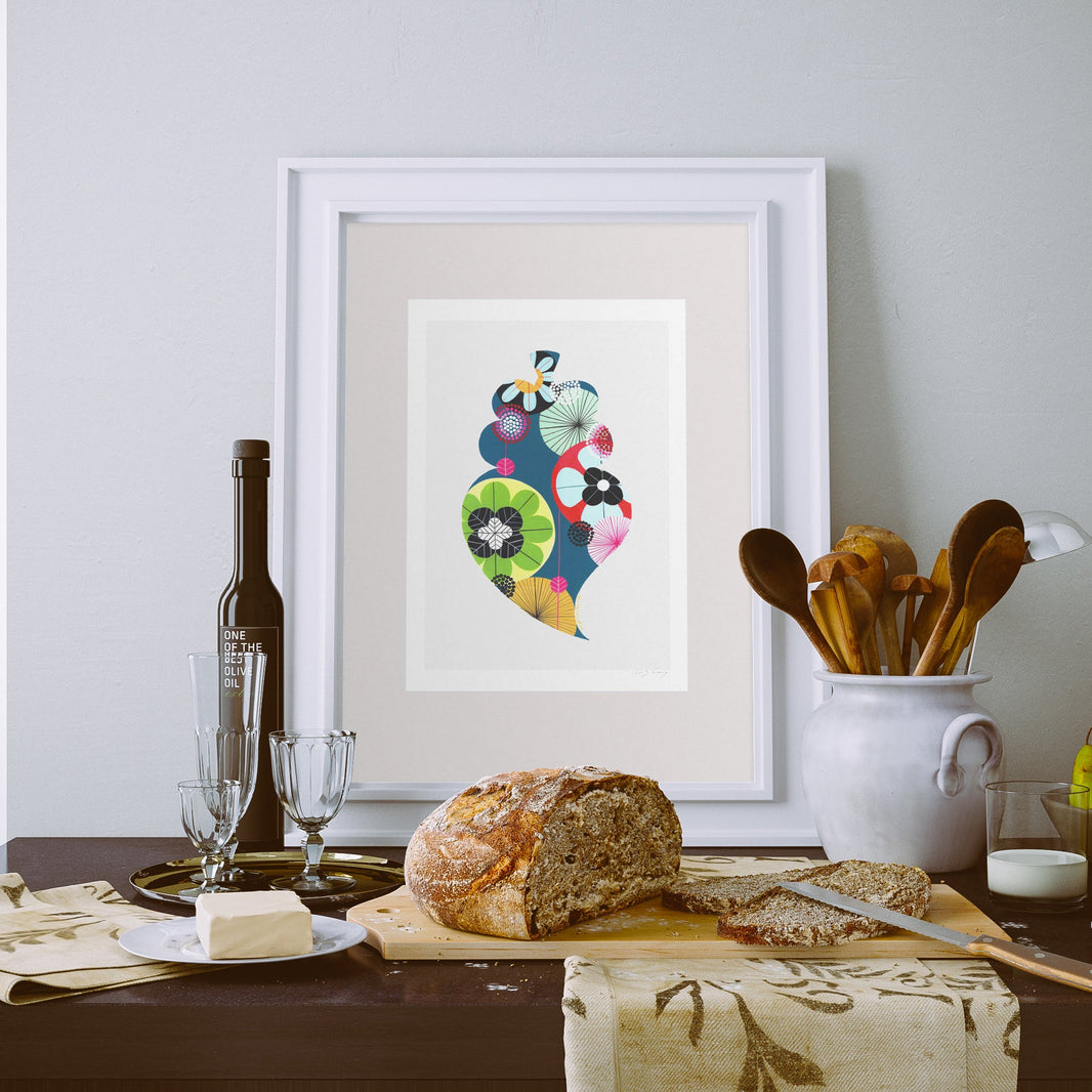 A framed fine art print, by Lis Gonçalves. Open edition, signed by the artist (printed in Hahnemühle matt fibre paper) featuring a colorful Portuguese Viana heart, displayed on a dining table with bread, butter, wine glasses, and wooden utensils.
