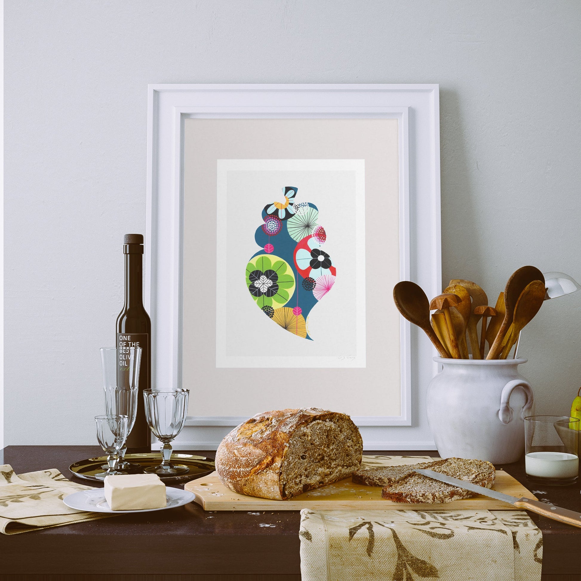 A framed fine art print, by Lis Gonçalves. Open edition, signed by the artist (printed in Hahnemühle matt fibre paper) featuring a colorful Portuguese Viana heart, displayed on a dining table with bread, butter, wine glasses, and wooden utensils.