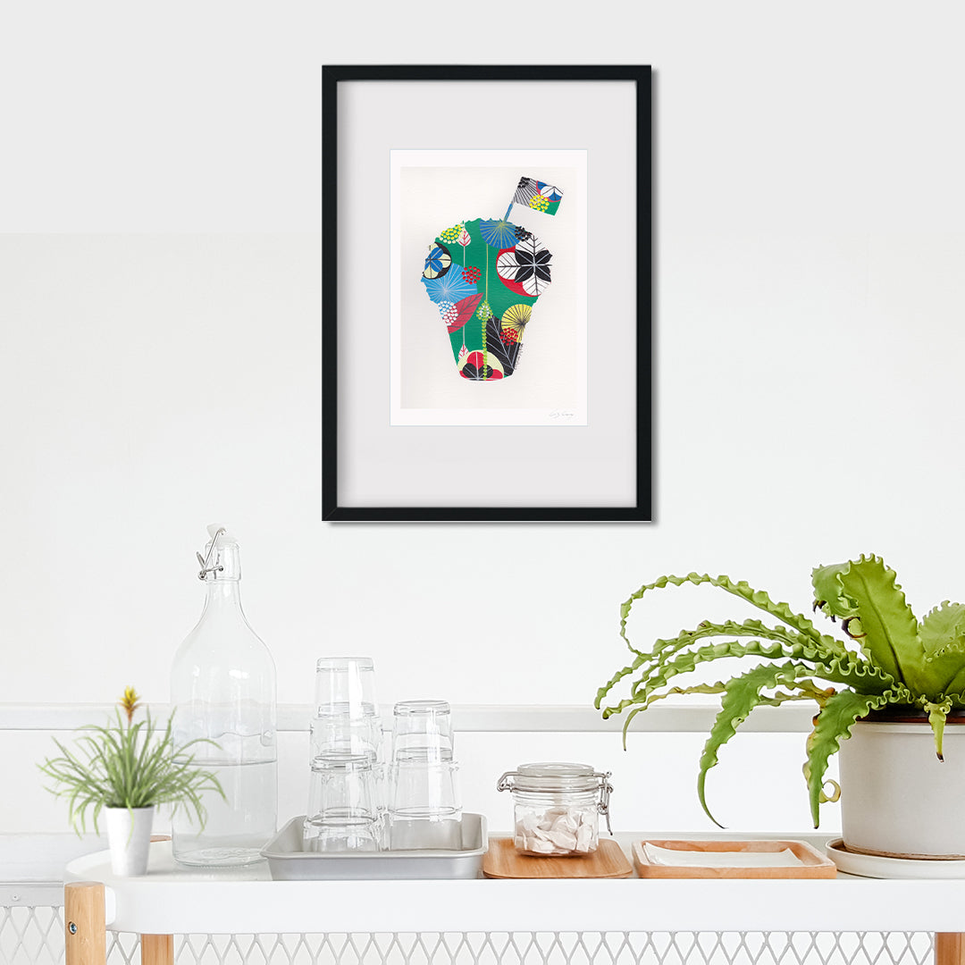 A framed fine art print, by Lis Gonçalves. Open edition, signed by the artist (printed in Hahnemühle matt fibre paper) featuring a colorful manjerico plant on a white wall above a kitchen counter.