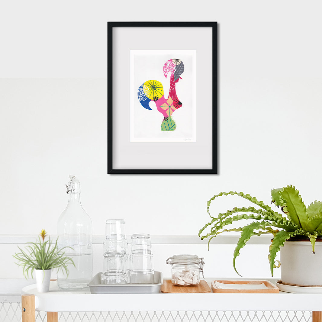 A framed fine art print, by Lis Gonçalves. Open edition, signed by the artist (printed in Hahnemühle matt fibre paper) featuring a colorful Portuguese rooster on a wall above a white shelf with plants and decor.