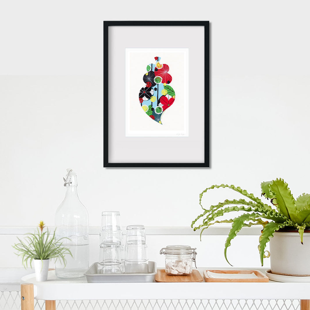 A framed fine art print, by Lis Gonçalves. Open edition, signed by the artist (printed in Hahnemühle matt fibre paper) featuring a colorful Portuguese Viana heart on a white wall with plants and decor below.