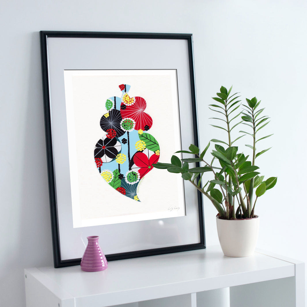 A framed fine art print, by Lis Gonçalves. Open edition, signed by the artist (printed in Hahnemühle matt fibre paper) featuring a colorful Portuguese Viana heart on a white surface with a plant and small vase.