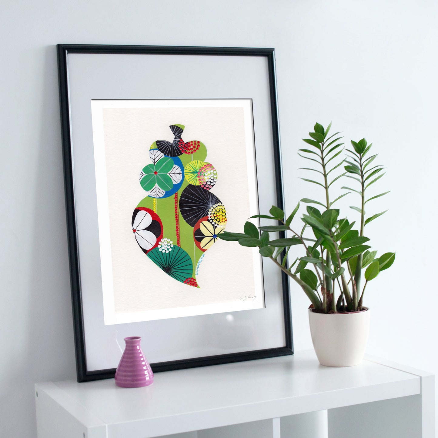 A framed fine art print, by Lis Gonçalves. Open edition, signed by the artist (printed in Hahnemühle matt fibre paper) featuring a colorful Portuguese Viana heart on a white surface with a plant and small vase.