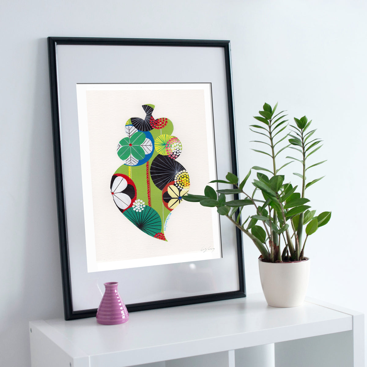 A framed fine art print, by Lis Gonçalves. Open edition, signed by the artist (printed in Hahnemühle matt fibre paper) featuring a colorful Portuguese Viana heart on a white surface with a plant and small vase.