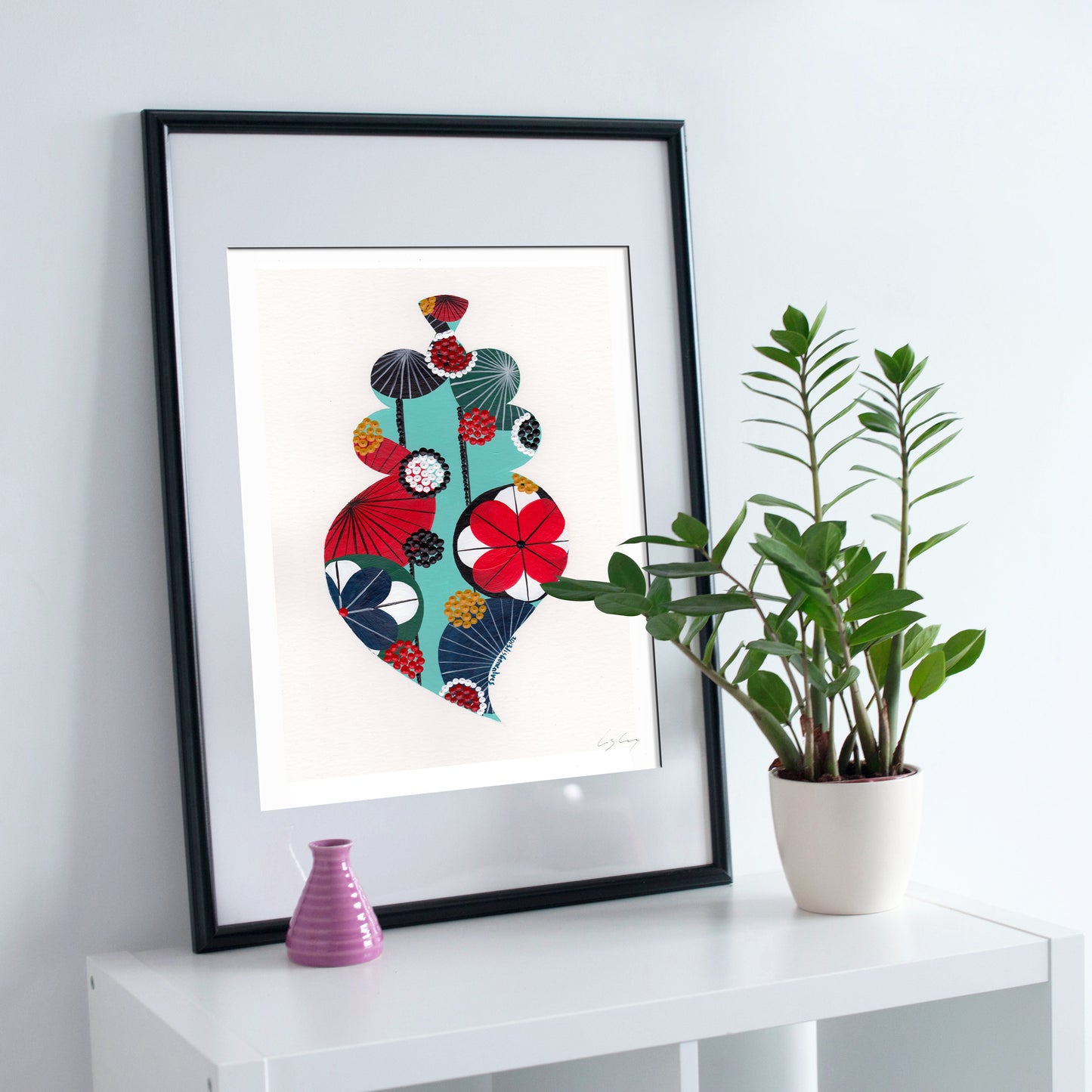 A framed fine art print, by Lis Gonçalves. Open edition, signed by the artist (printed in Hahnemühle matt fibre paper) featuring a colorful Portuguese Viana heart on a white surface with a plant and small vase.