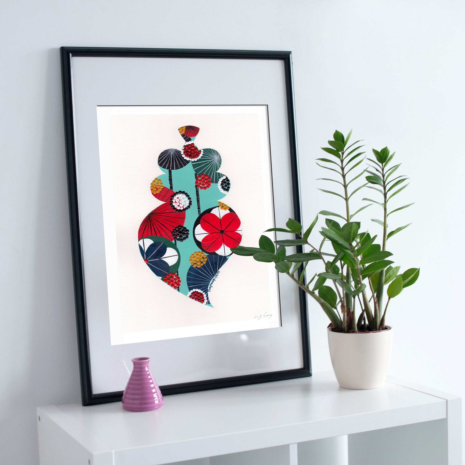 A framed fine art print, by Lis Gonçalves. Open edition, signed by the artist (printed in Hahnemühle matt fibre paper) featuring a colorful Portuguese Viana heart on a white surface with a plant and small vase.