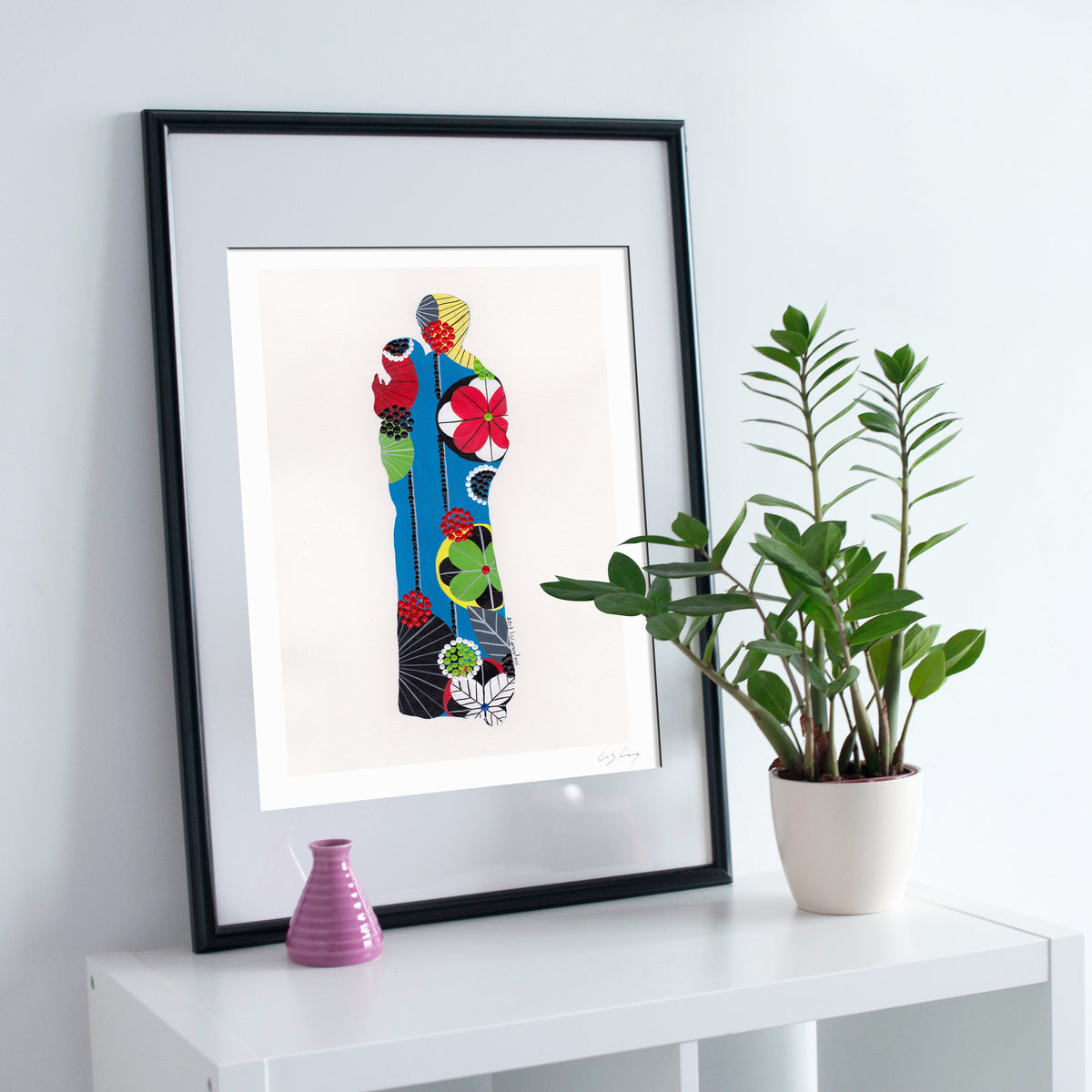A framed fine art print, by Lis Gonçalves. Open edition, signed by the artist (printed in Hahnemühle matt fibre paper) featuring a colorful Saint Anthony on a white surface with a plant and small vase.