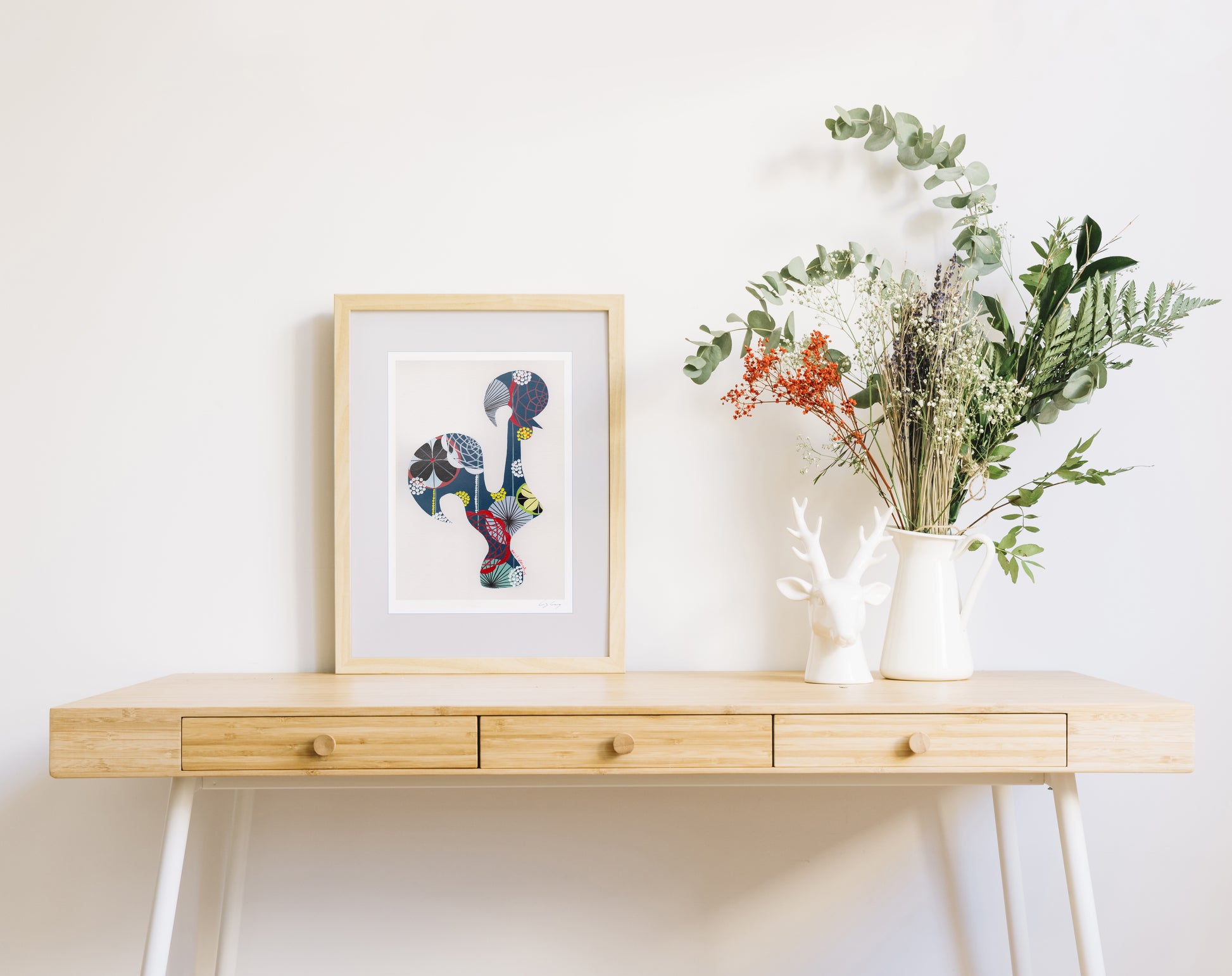 A framed fine art print, by Lis Gonçalves. Open edition, signed by the artist (printed in Hahnemühle matt fibre paper) featuring a colorful Portuguese rooster over a wooden table with decorative items.