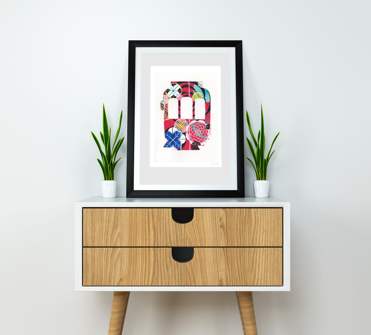 A framed fine art print, by Lis Gonçalves. Open edition, signed by the artist (printed in Hahnemühle matt fibre paper) featuring a colorful Lisbon tram on a wooden side table with two potted plants.