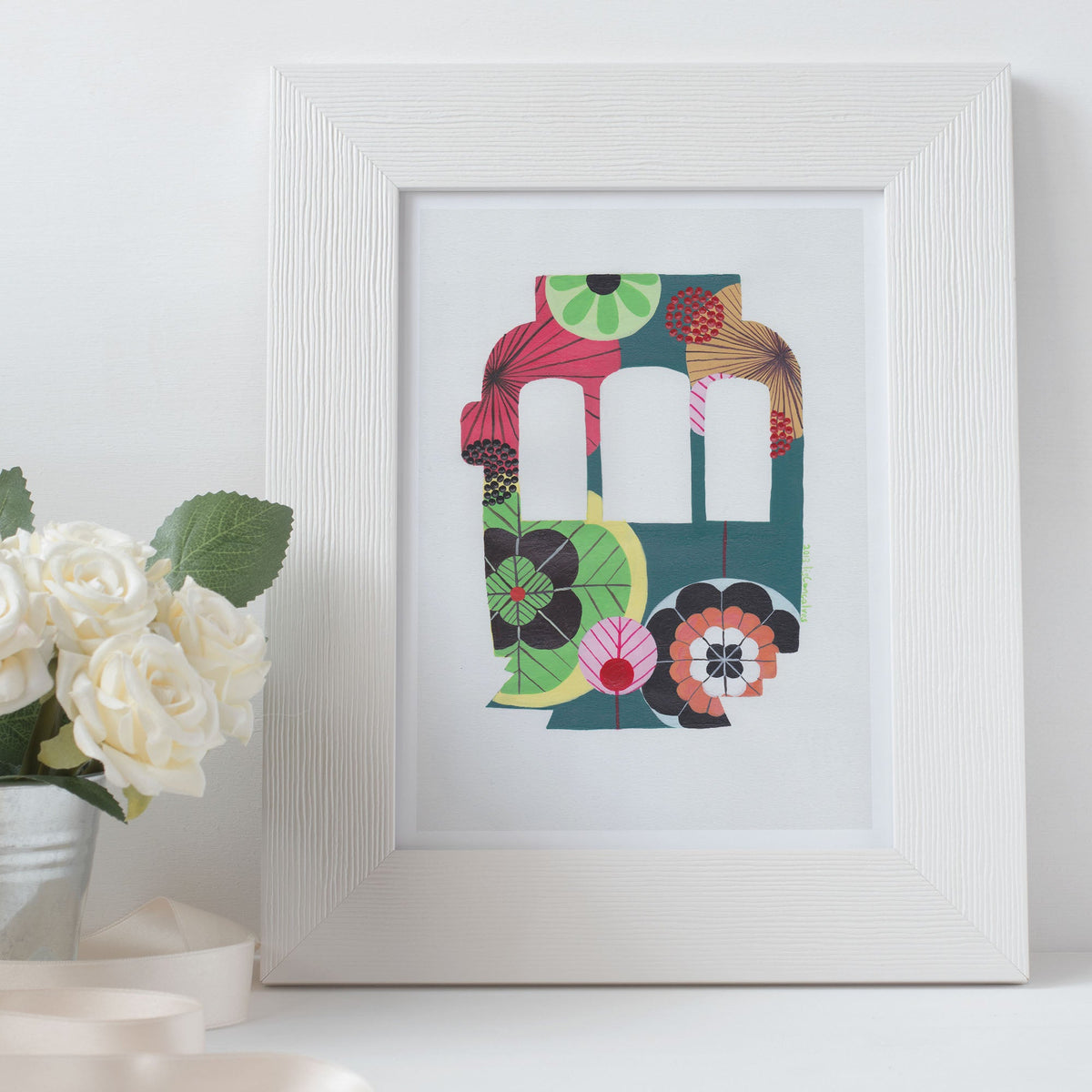 A framed fine art print, by Lis Gonçalves. Open edition, signed by the artist (printed in Hahnemühle matt fibre paper) featuring a colorful Lisbon tram on a white surface with a potted plant.