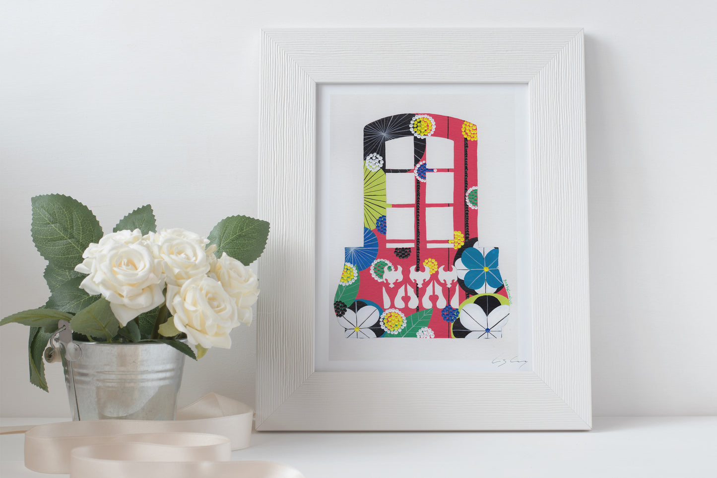 A framed fine art print, by Lis Gonçalves. Open edition, signed by the artist. Printed in Hahnemühle matt fibre paper; featuring a colorful balcony with flowers on a white surface next to a potted plant.