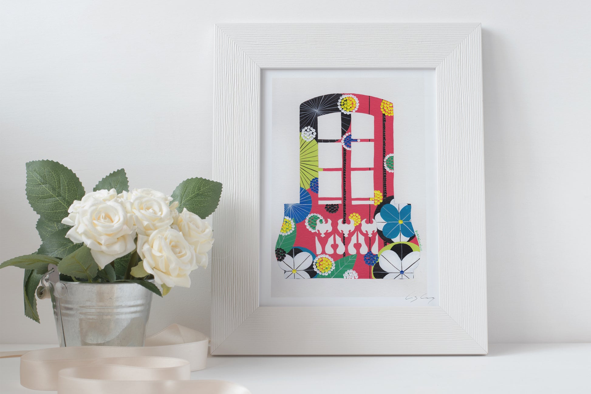 A framed fine art print, by Lis Gonçalves. Open edition, signed by the artist. Printed in Hahnemühle matt fibre paper; featuring a colorful balcony with flowers on a white surface next to a potted plant.
