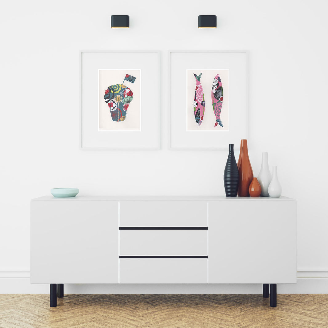 Two framed fine art prints, by Lis Gonçalves. Open edition, signed by the artist (printed in Hahnemühle matt fibre paper) featuring a manjerico and sardines, over a white cabinet with decorative items.