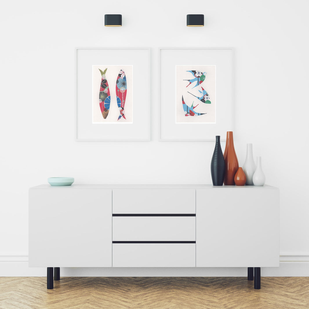 Two framed fine art prints, by Lis Gonçalves. Open edition, signed by the artist (printed in Hahnemühle matt fibre paper) featuring colorful swallows and sardines in a modern interior with a white cabinet and decorative vases.