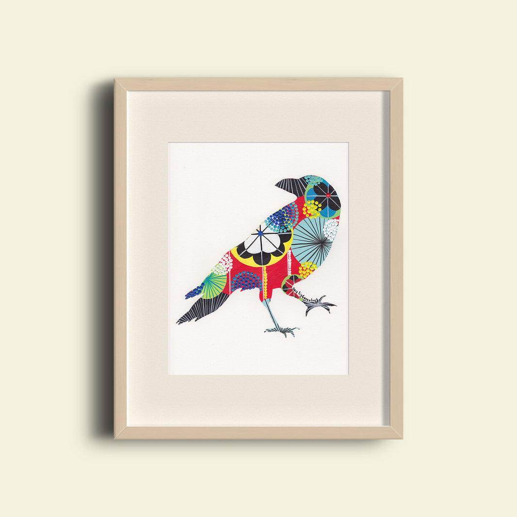 A framed fine art print, by Lis Gonçalves. Open edition, signed by the artist. Printed in Hahnemühle matt fibre paper; of a colorful bird design on a beige wall