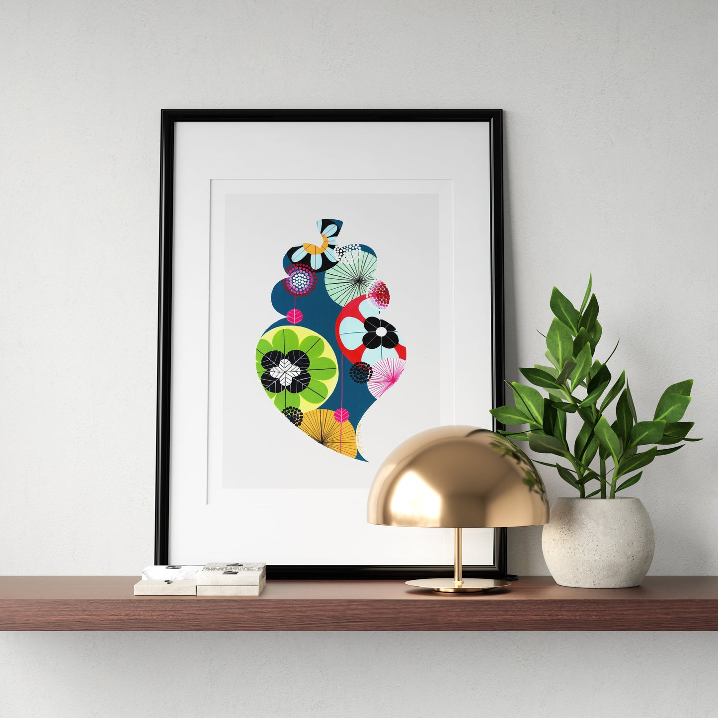 A framed fine art print, by Lis Gonçalves. Open edition, signed by the artist (printed in Hahnemühle matt fibre paper) featuring a colorful Portuguese Viana heart, styled on a wooden shelf next to a gold dome lamp and a potted green plant against a light gray wall.