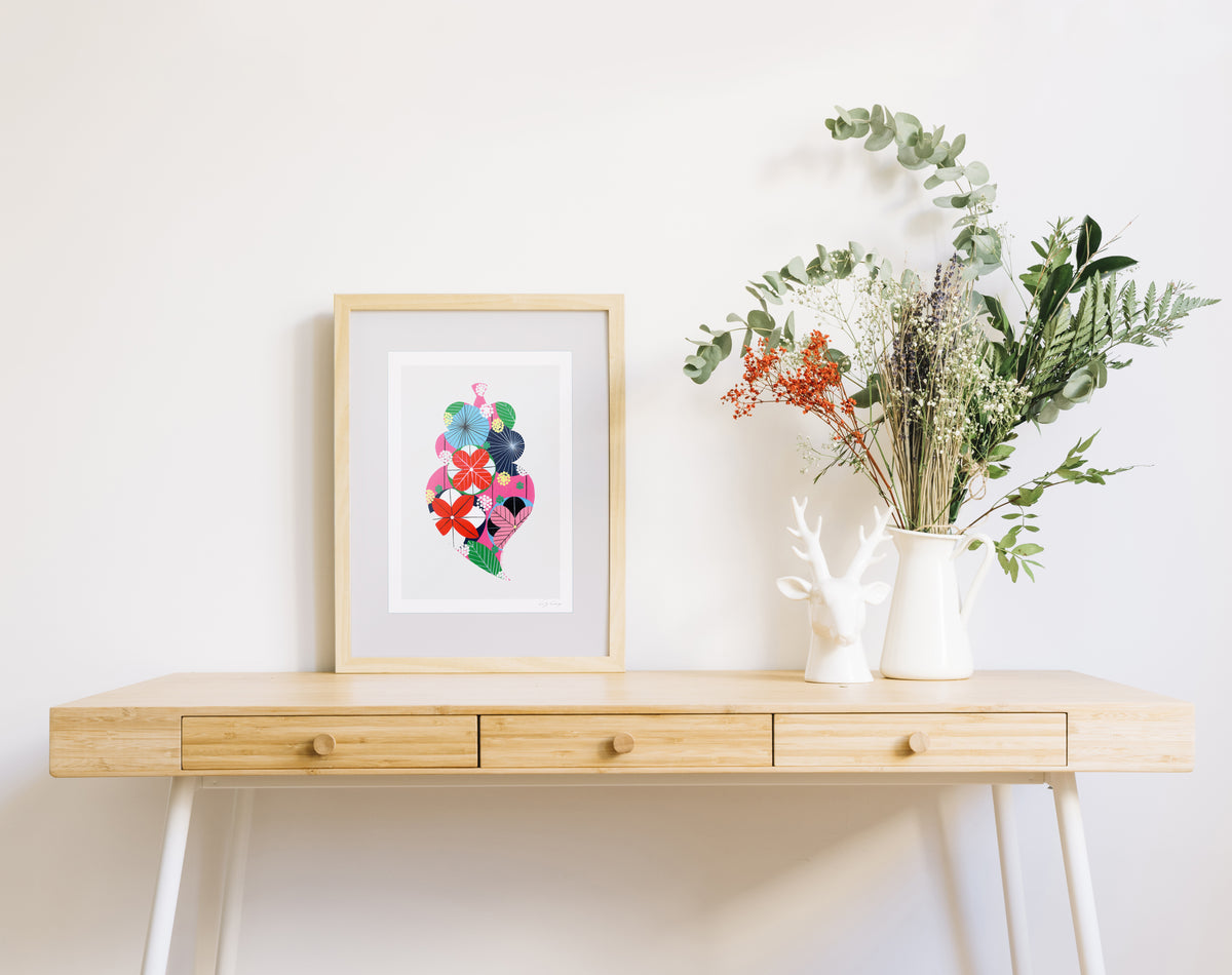 A framed fine art print, by Lis Gonçalves. Open edition, signed by the artist (printed in Hahnemühle matt fibre paper) featuring a colorful Portuguese Viana heart on a wooden table with a vase of flowers on a white background