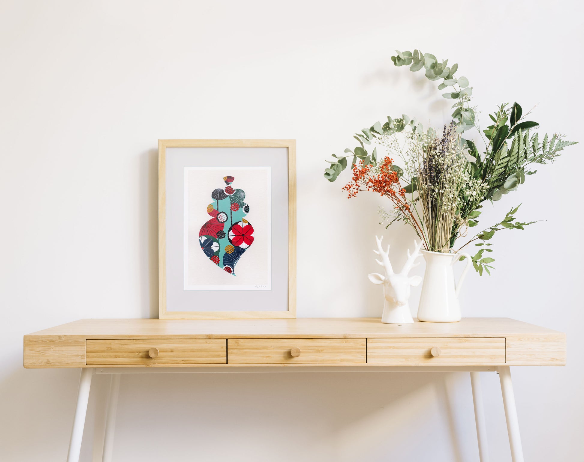 A framed fine art print, by Lis Gonçalves. Open edition, signed by the artist (printed in Hahnemühle matt fibre paper) featuring a colorful Portuguese Viana heart  on a wooden desk with a vase of flowers on a white background