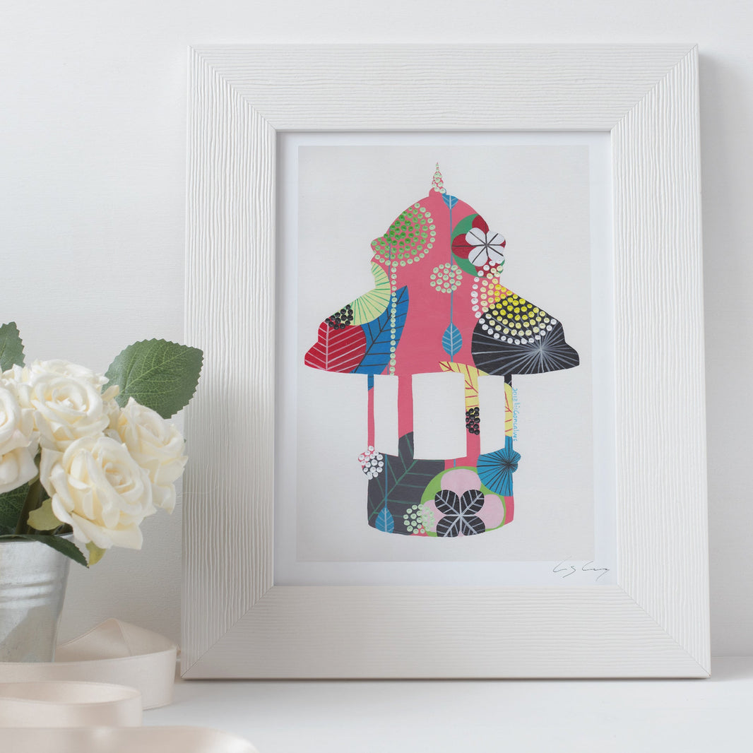 A framed fine art print, by Lis Gonçalves. Open edition, signed by the artist (printed in Hahnemühle matt fibre paper) featuring a colorful Lisbon kiosk on a white surface with flowers.