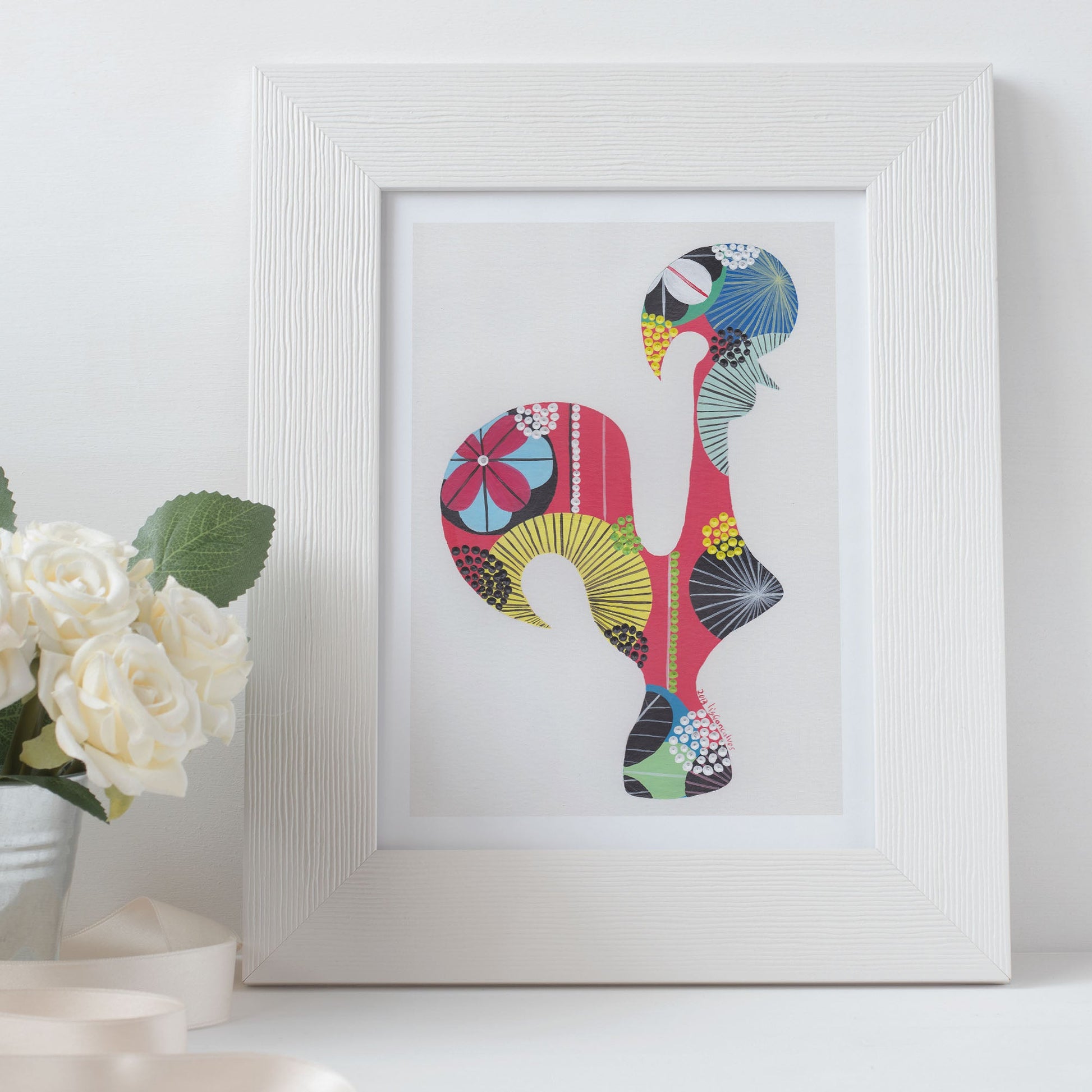 A framed fine art print, by Lis Gonçalves. Open edition, signed by the artist (printed in Hahnemühle matt fibre paper) featuring a colorful Portuguese rooster in a white frame with roses in a white background.