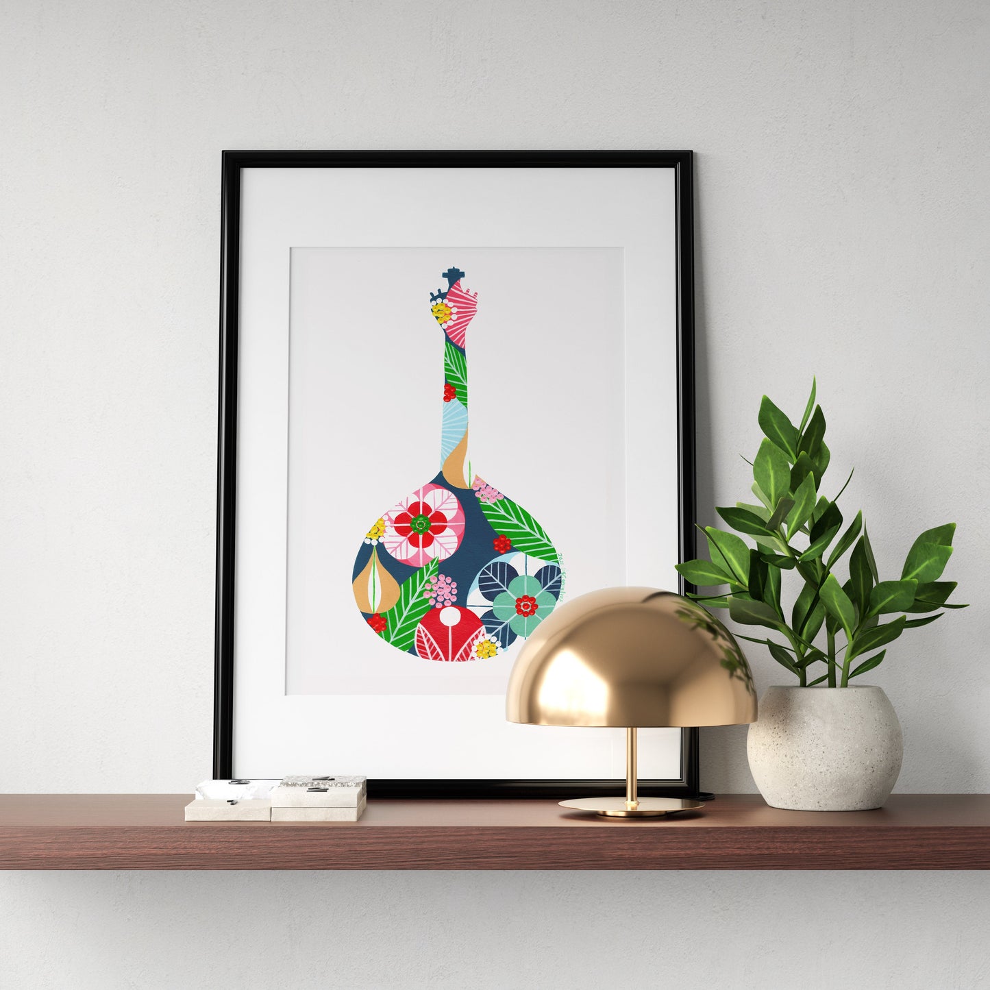 A framed fine art print, by Lis Gonçalves. Open edition, signed by the artist (printed in Hahnemühle matt fibre paper) featuring a colorful Portuguese guitar, on a wooden shelf with a lamp and plant.