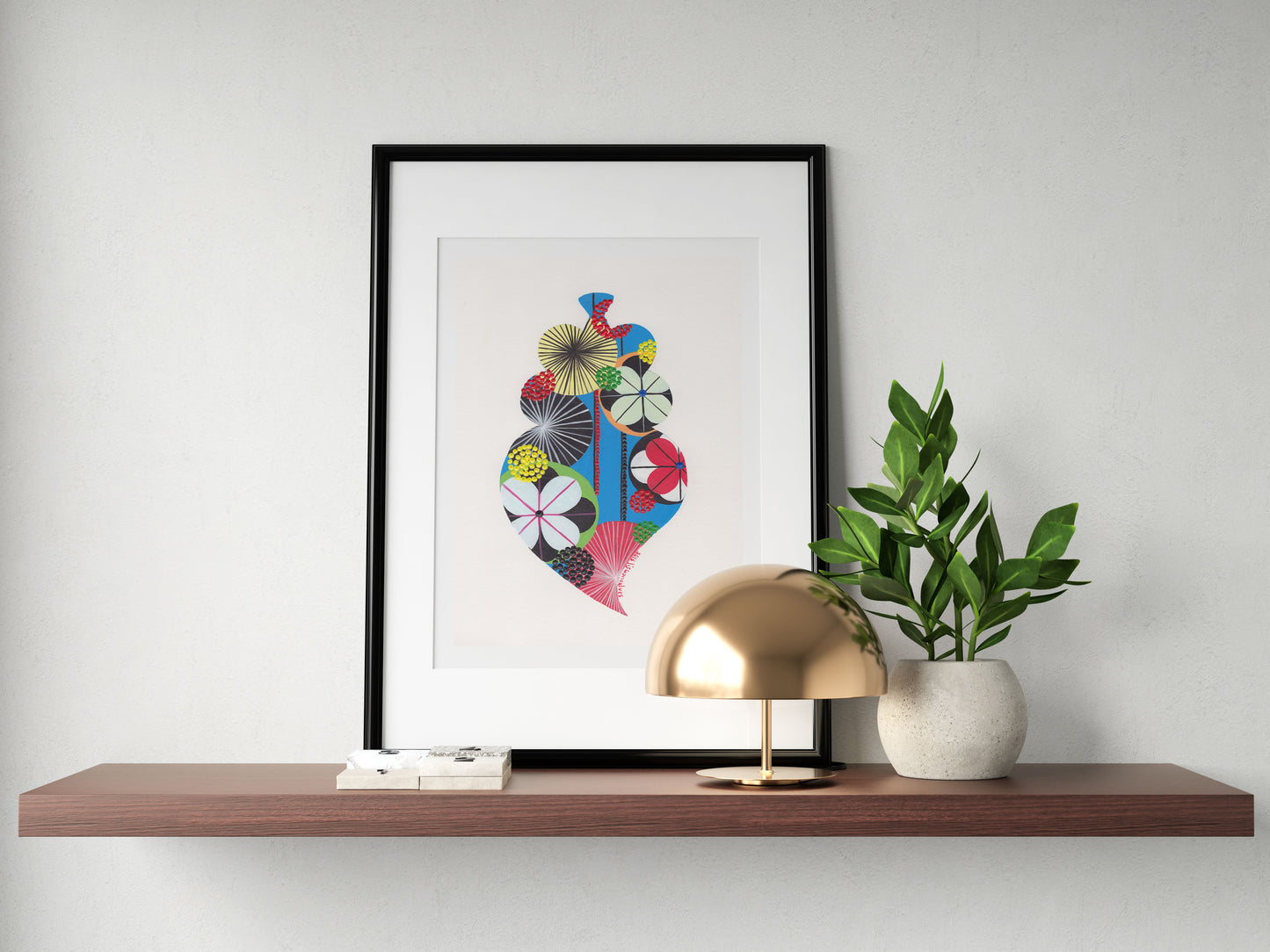 A framed fine art print, by Lis Gonçalves. Open edition, signed by the artist (printed in Hahnemühle matt fibre paper) featuring a colorful Portuguese Viana heart on a wooden shelf with a lamp and plant against a white wall.