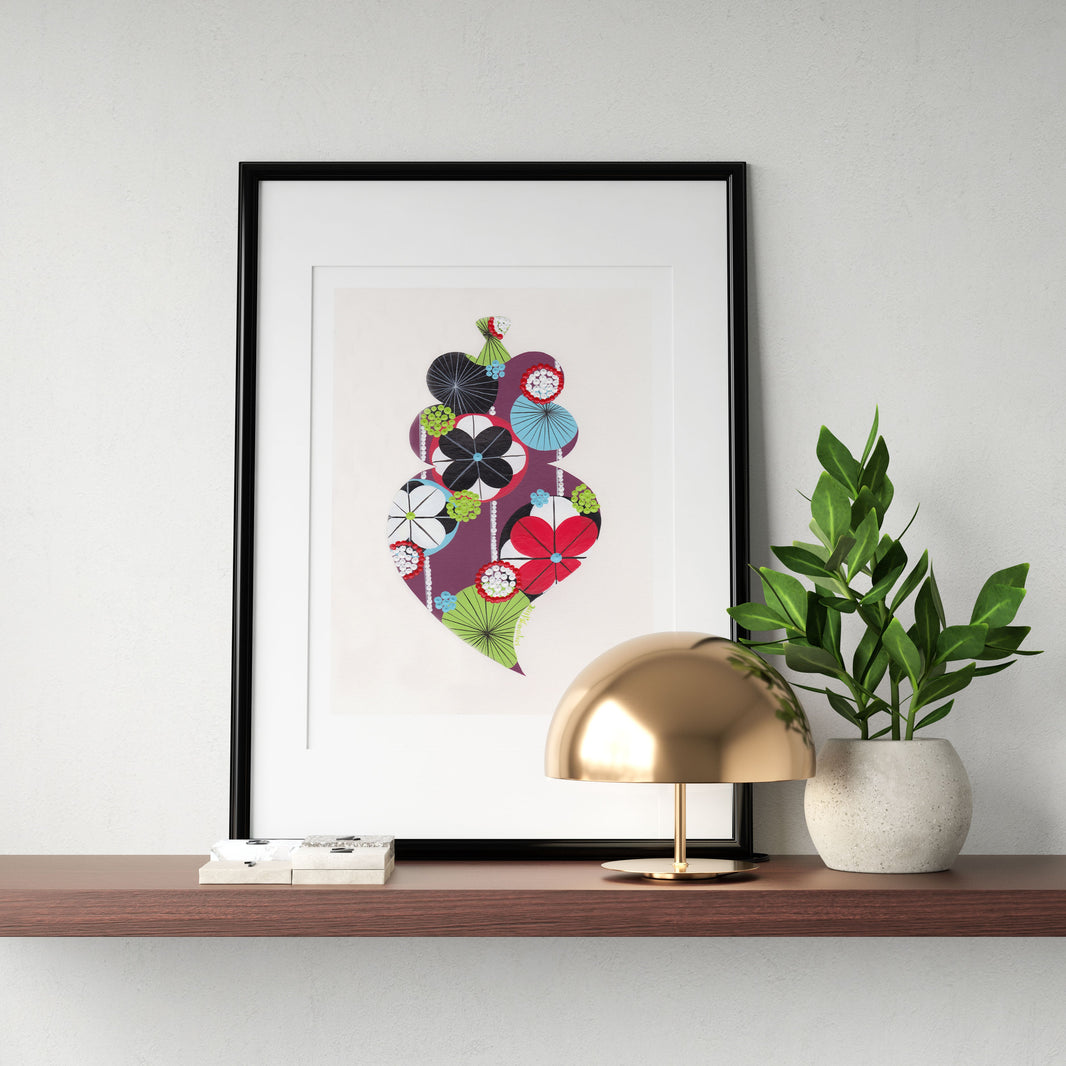 A framed fine art print, by Lis Gonçalves. Open edition, signed by the artist (printed in Hahnemühle matt fibre paper) featuring a colorful Portuguese Viana heart on a wooden shelf with a lamp and plant against a white wall.