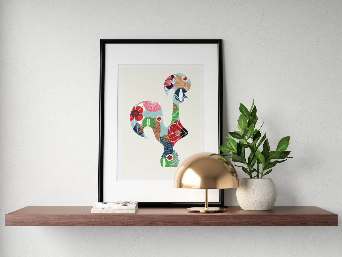 A framed fine art print, by Lis Gonçalves. Open edition, signed by the artist (printed in Hahnemühle matt fibre paper) featuring a colorful Portuguese rooster on a wooden shelf with a lamp and plant.