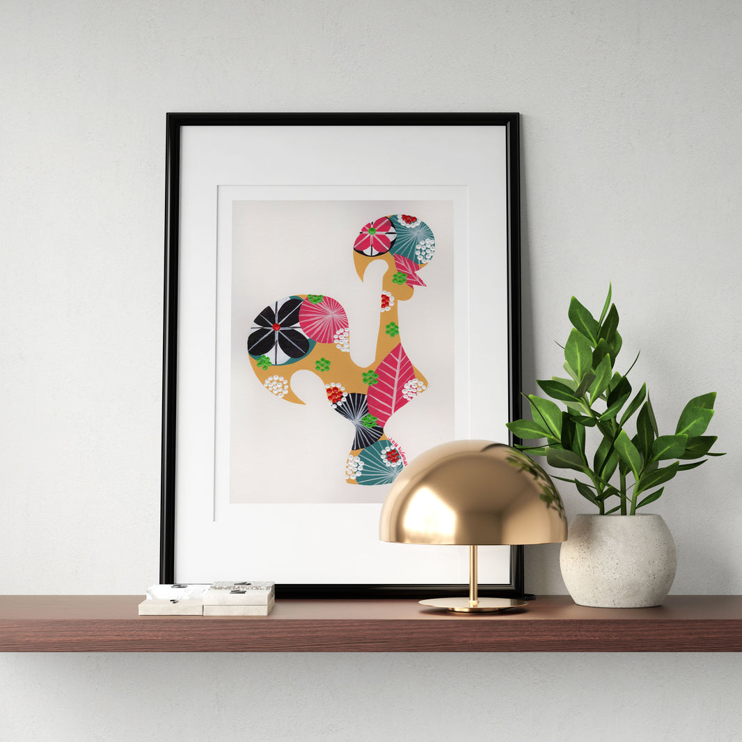 A framed fine art print, by Lis Gonçalves. Open edition, signed by the artist (printed in Hahnemühle matt fibre paper) featuring a colorful Portuguese rooster on a shelf with a gold lamp, and green plant on a white wall.