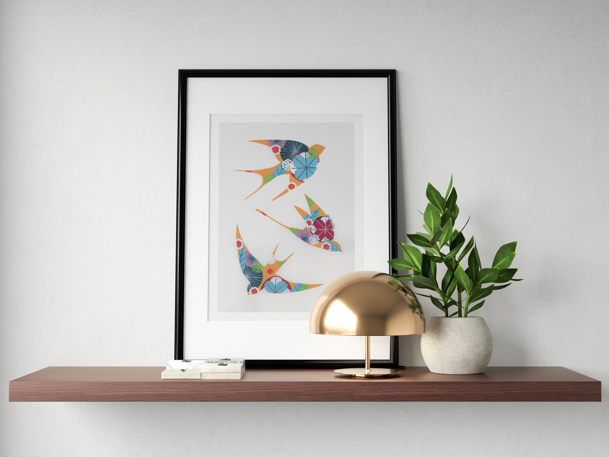 A framed fine art print, by Lis Gonçalves. Open edition, signed by the artist (printed in Hahnemühle matt fibre paper) featuring colorful swallows on a wall above a wooden shelf with a lamp and plant.