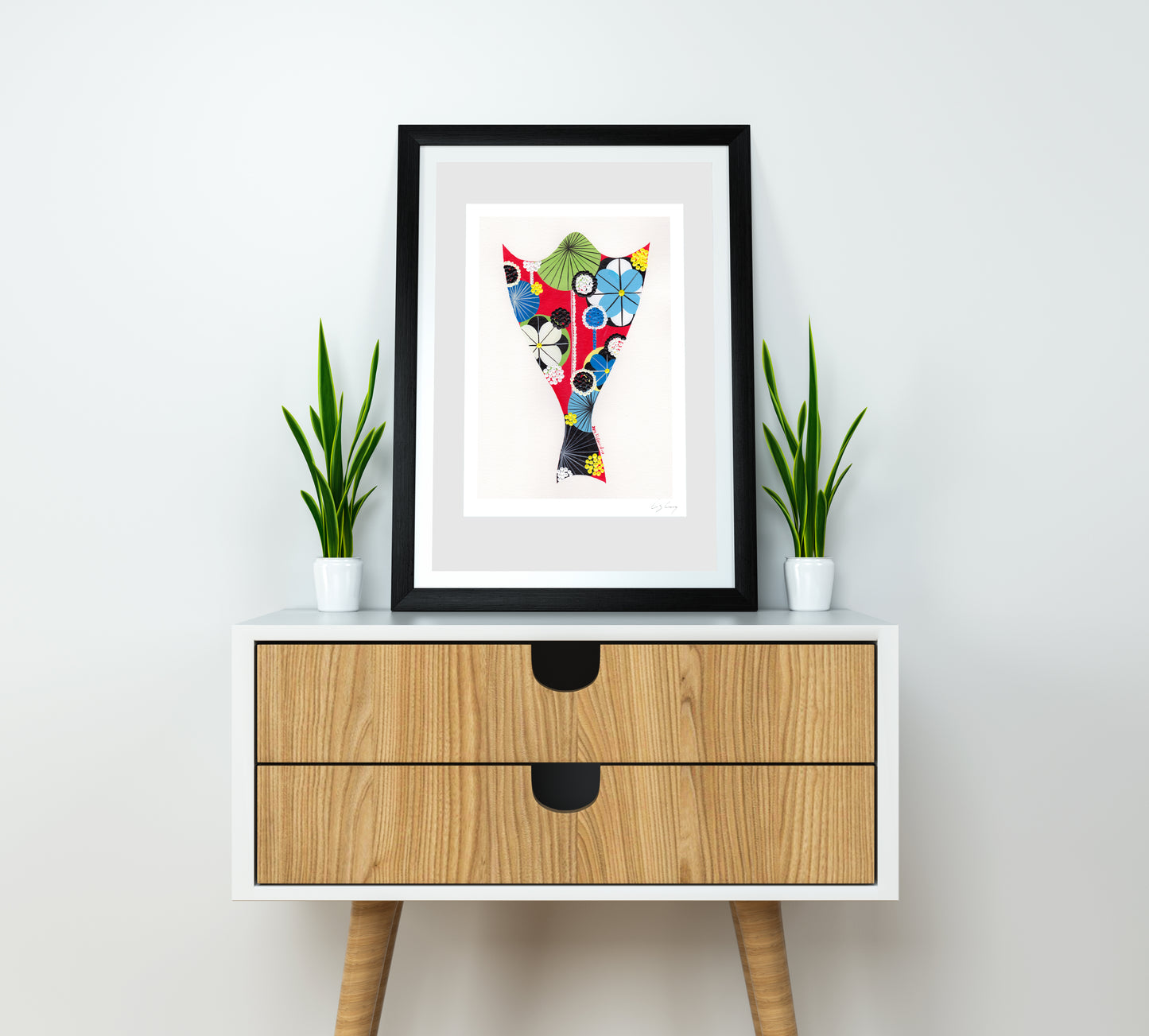 A framed fine art print, by Lis Gonçalves. Open edition, signed by the artist (printed in Hahnemühle matt fibre paper) featuring a bacalhau illustration on a white wall above a wooden cabinet with plants.