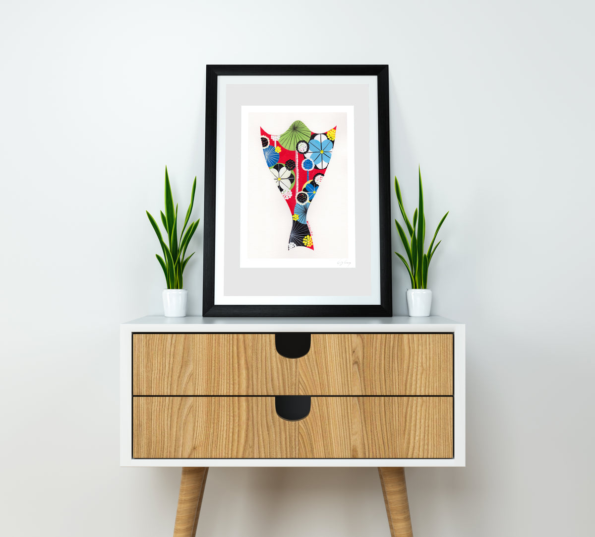 A framed fine art print, by Lis Gonçalves. Open edition, signed by the artist (printed in Hahnemühle matt fibre paper) featuring a bacalhau illustration on a white wall above a wooden cabinet with plants.