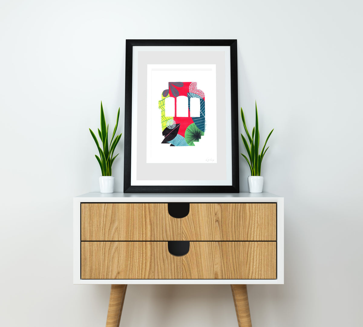 A framed fine art print, by Lis Gonçalves. Open edition, signed by the artist (printed in Hahnemühle matt fibre paper) featuring a colorful Lisbon tram on a wooden side table with plants against a white wall.
