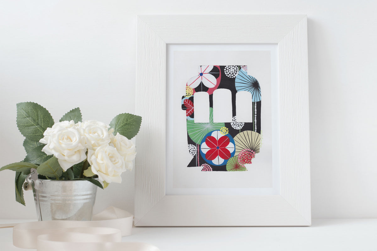 A framed fine art print, by Lis Gonçalves. Open edition, signed by the artist (printed in Hahnemühle matt fibre paper) featuring a colorful Lisbon tram on a white surface with flowers.