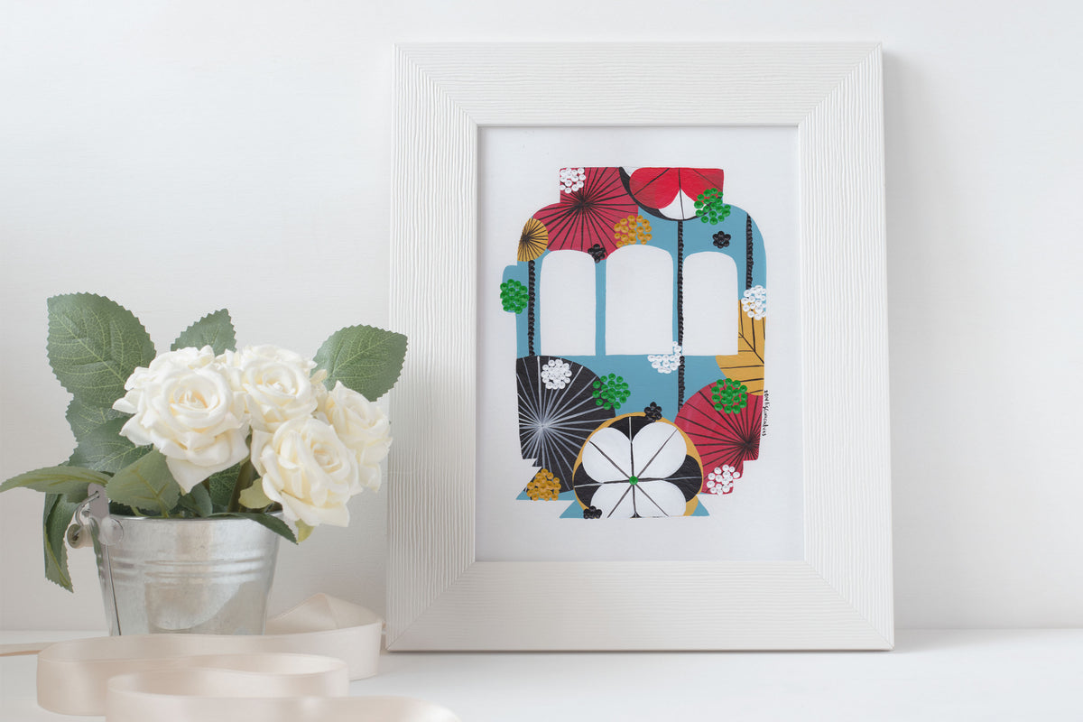 A framed fine art print, by Lis Gonçalves. Open edition, signed by the artist (printed in Hahnemühle matt fibre paper) featuring a colorful Lisbon tram on a white surface with flowers.