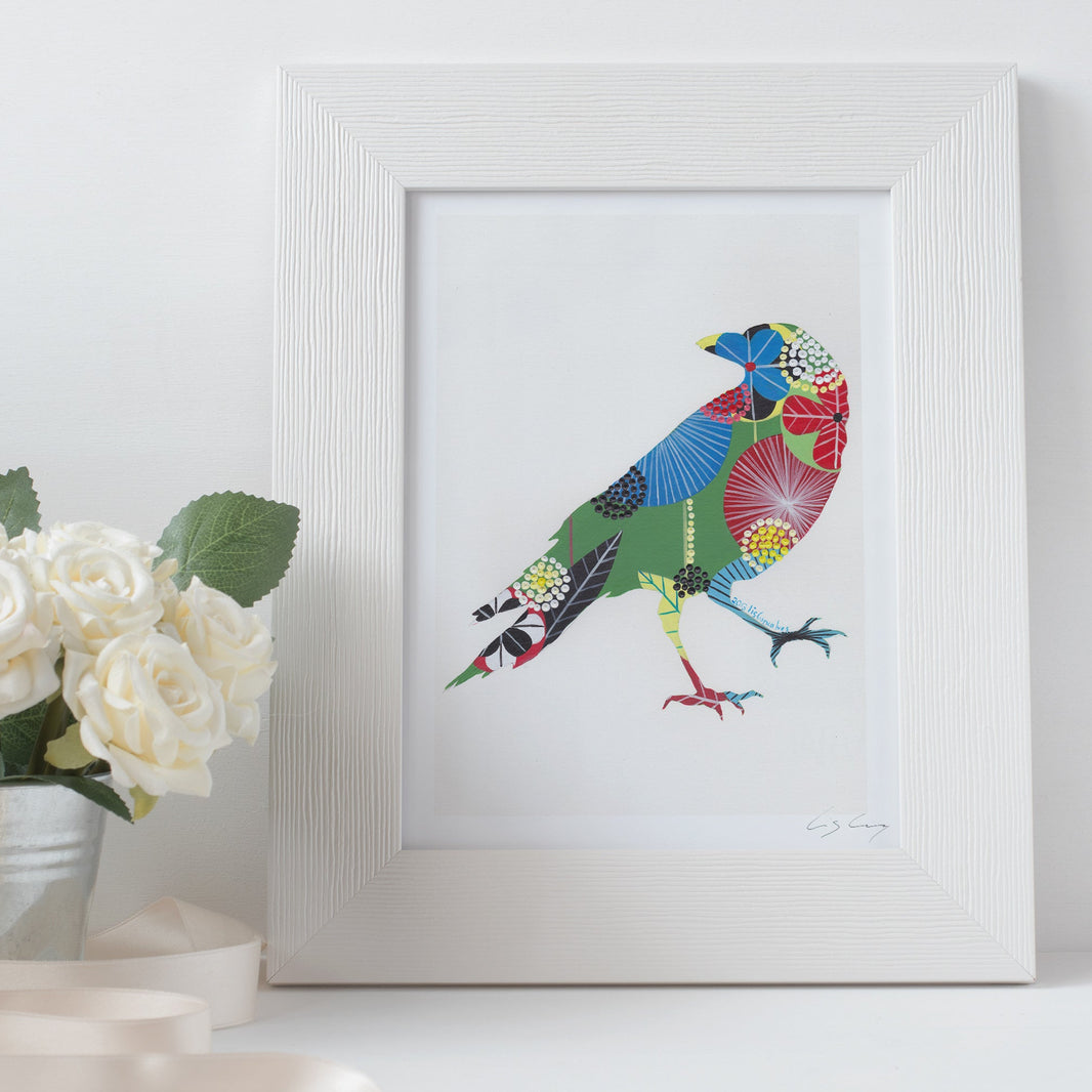 A framed fine art print, by Lis Gonçalves. Open edition, signed by the artist (printed in Hahnemühle matt fibre paper) of a colorful raven on a white surface with flowers.
